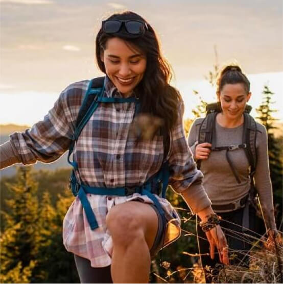 Two people hike along a forested trail at sunset, their backpacks snug and outdoor clothing fit for the adventure, capturing the serenity and natural beauty that Suncadia is renowned for.