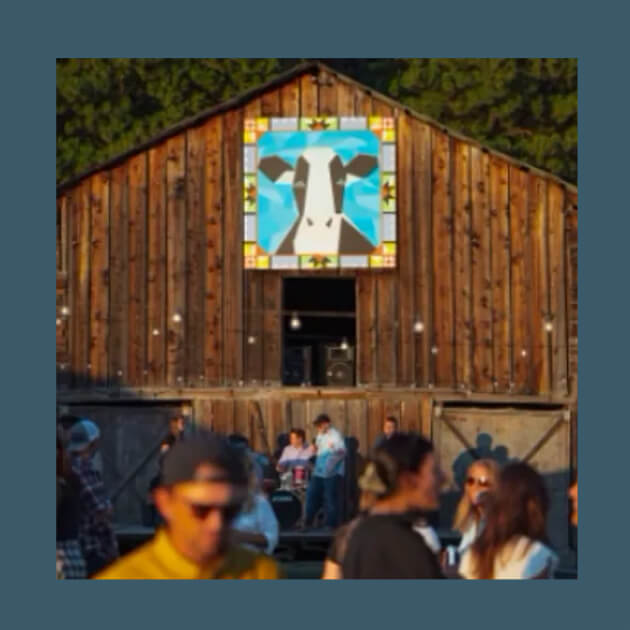 People gather in front of a rustic barn with a colorful cow mural under the clear sky at Suncadia Resort, enjoying the picturesque setting of this Washington gem.