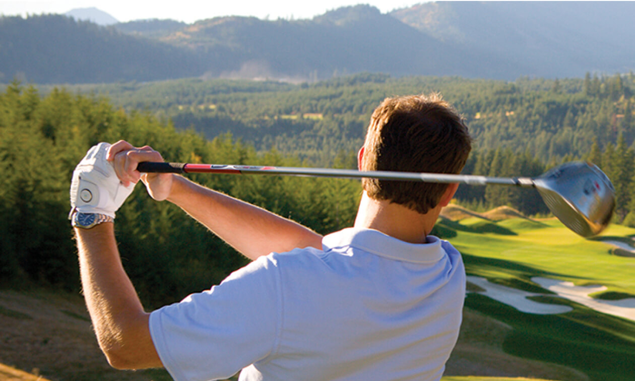 A golfer follows through on a swing at Suncadia, facing a scenic view of the lush golf course and distant mountains, epitomizing the charm of Suncadia real estate.