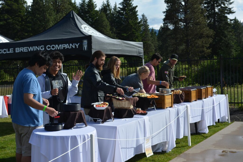 a group of people standing around a table with food on it.