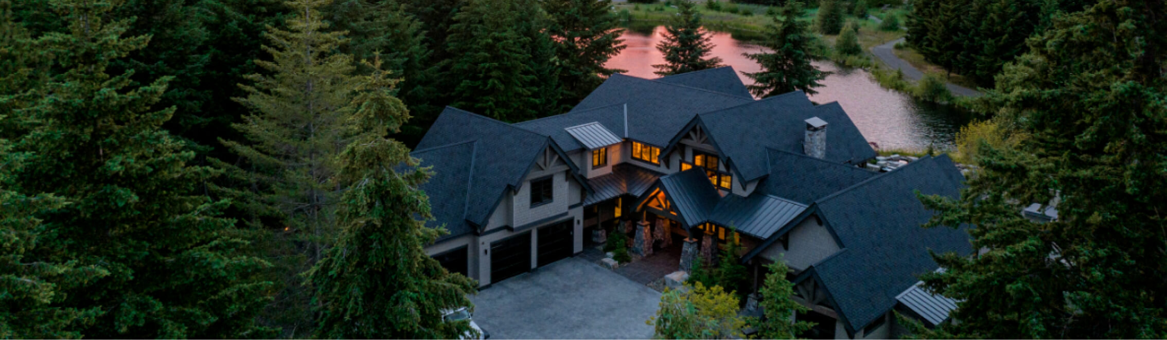 A large Suncadia home with dark roofing is surrounded by trees near a lake at sunset, embodying the serene beauty Suncadia Resort offers.