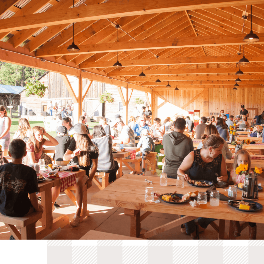 People gathered at wooden picnic tables under a pavilion, enjoying the vibrant atmosphere of Suncadia Resort Washington, as sunlight streamed through the open space, creating the perfect setting for eating and socializing.