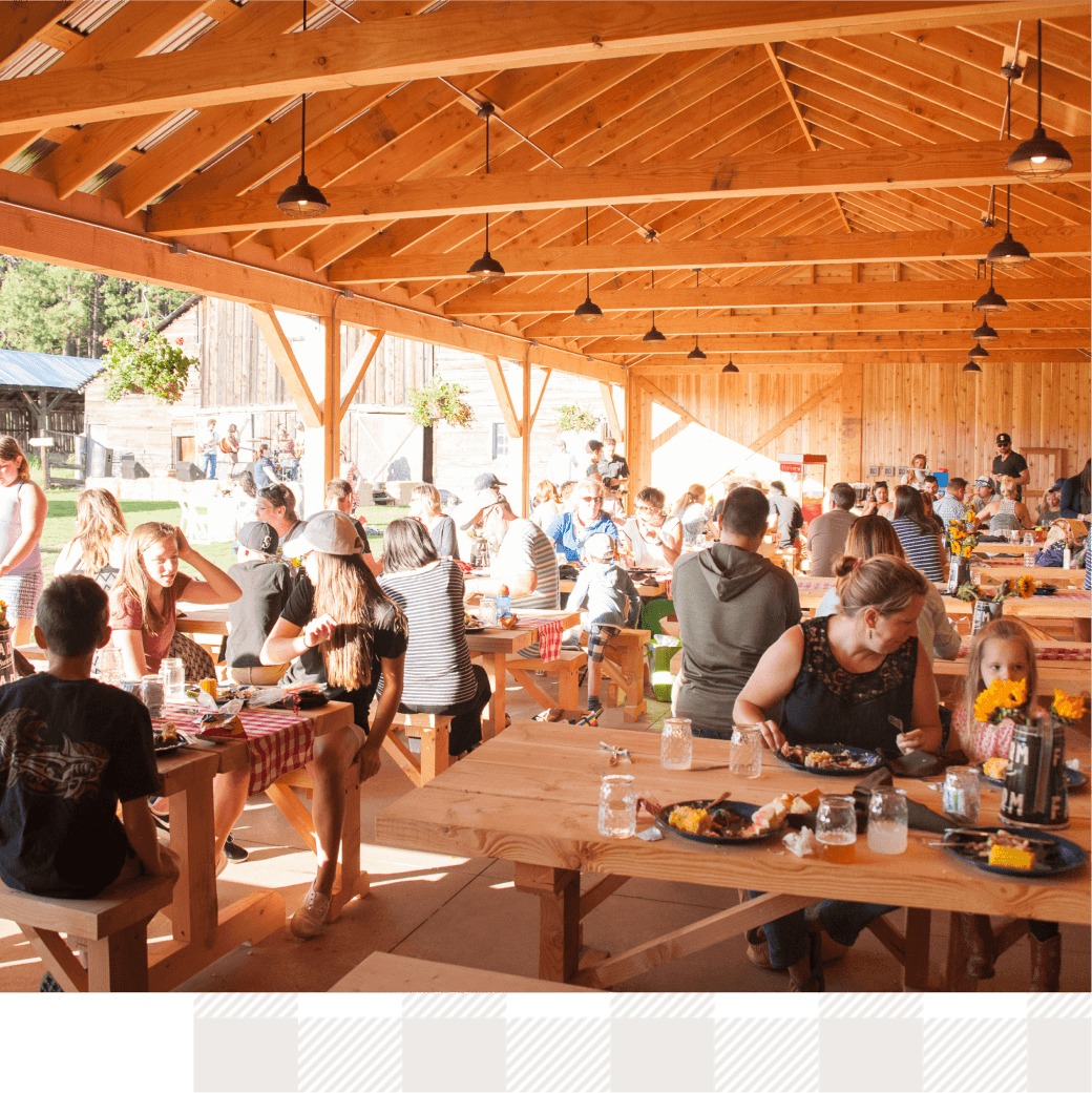 People gathered at wooden picnic tables under a pavilion, enjoying the vibrant atmosphere of Suncadia Resort Washington, as sunlight streamed through the open space, creating the perfect setting for eating and socializing.