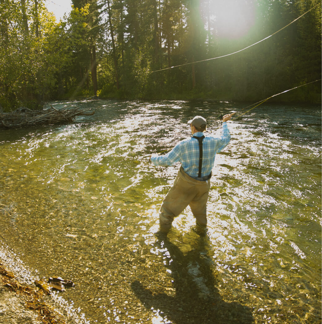 A person enjoys fly fishing in a sunlit river at Suncadia Resort, Washington, surrounded by lush trees. After a day on the water, they look forward to exploring Cle Elum restaurants for a delicious meal.