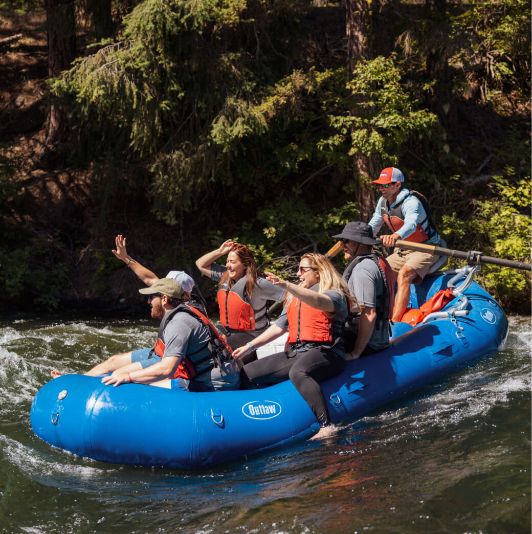 A group of people in life jackets are navigating a blue inflatable raft through rapids on a river, embraced by trees near Suncadia Resort, Washington.