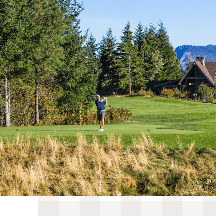 A person playing golf on a lush green course at Suncadia Resort, surrounded by trees with a charming house nestled in the background, offers a serene retreat near Cle Elum's delightful restaurants.