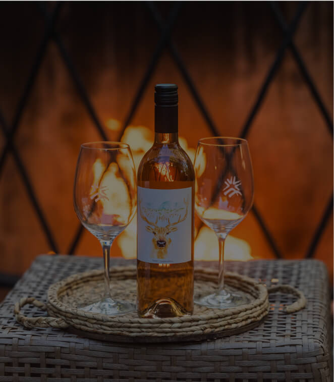 A bottle of wine and two empty glasses sit on a wicker tray in front of a fireplace, capturing the cozy ambiance often found at Suncadia Resort Washington.