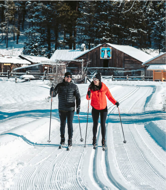 Two people cross-country skiing on a snowy trail in front of a rustic cabin surrounded by trees, enjoying the serene landscapes near Suncadia.