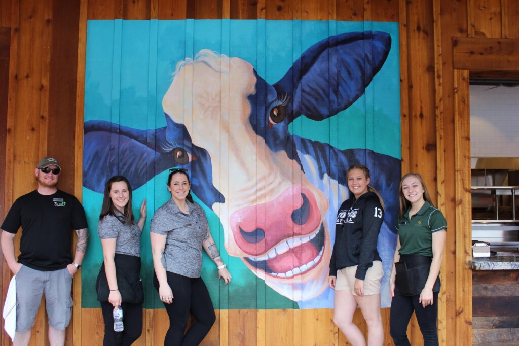 a group of people standing in front of a painting of a cow.