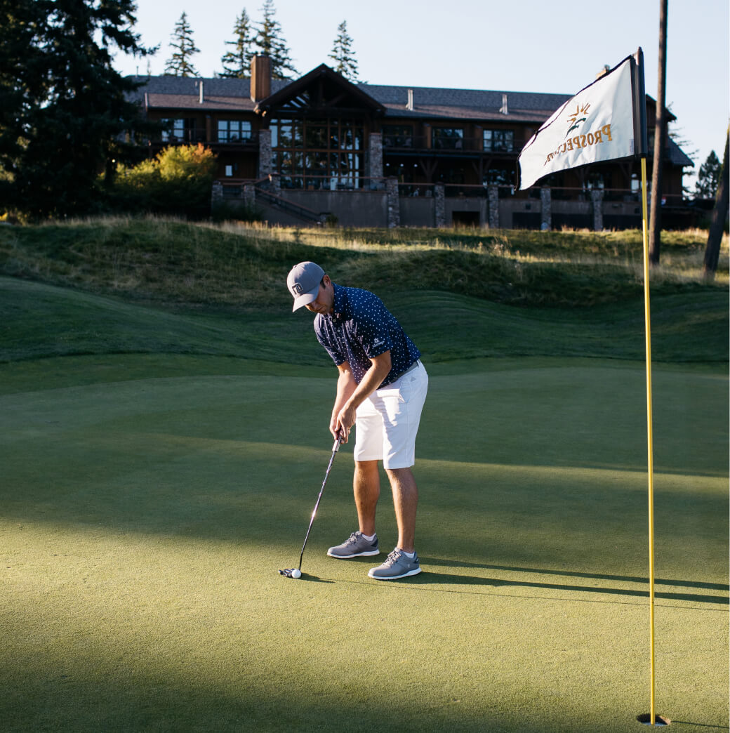 A golfer in a cap and shorts is putting on a sunlit green near a flag, with the elegant backdrop of Suncadia homes completing the picturesque scene.