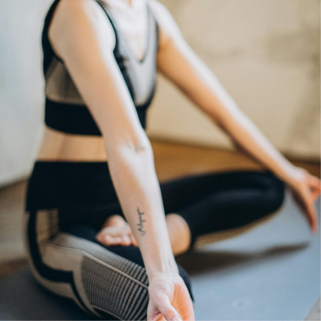 A person in a yoga pose sits cross-legged on a mat, wearing patterned athletic wear with a tattoo visible on their forearm. They're enjoying tranquility, much like the serene ambiance of Suncadia Resort in Washington.