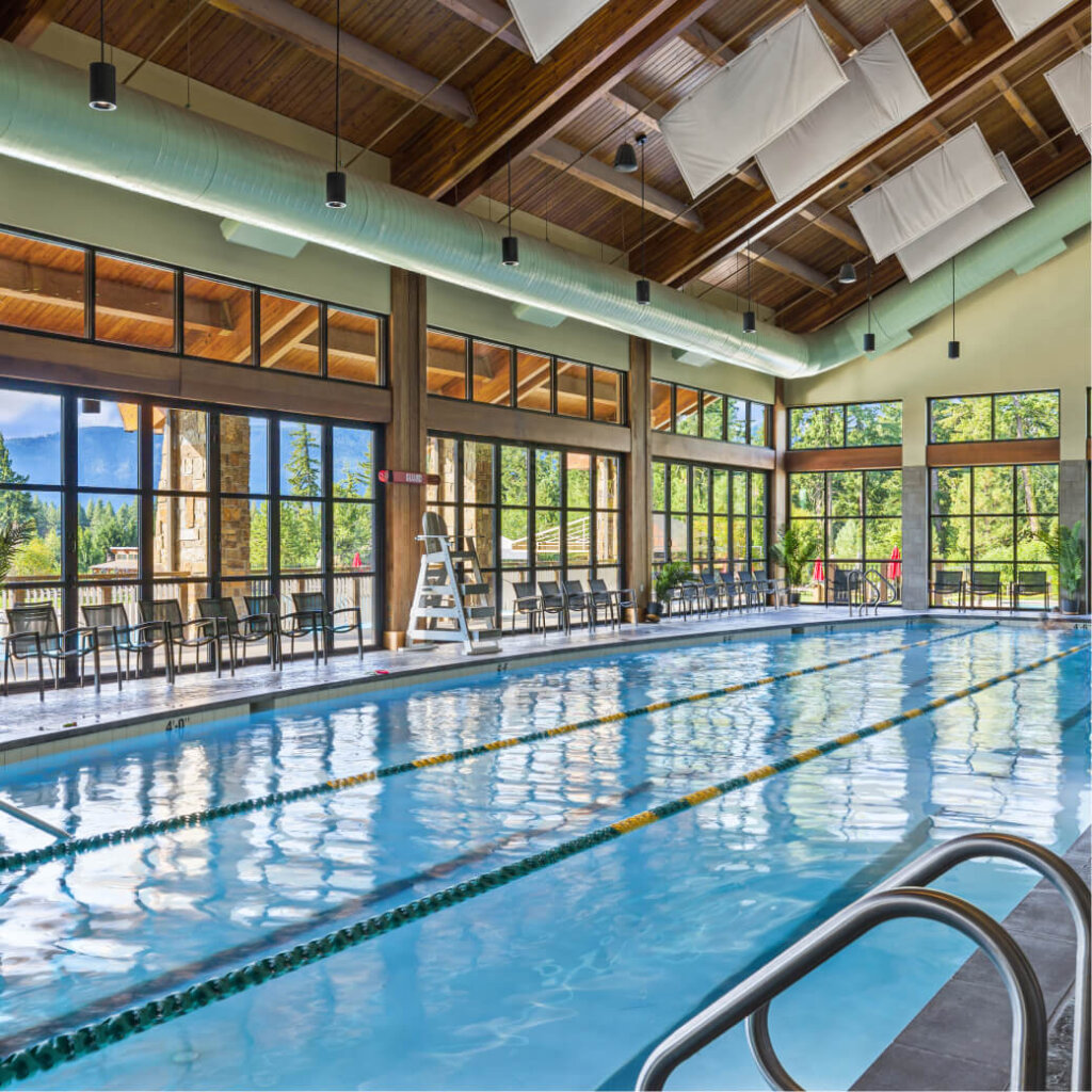 Indoor swimming pool with lap lanes at Suncadia Resort, Washington, surrounded by large windows and a wooden ceiling. Chairs line the walls, and a lifeguard stand is visible. Enjoy nearby Cle Elum restaurants for a complete experience in this beautiful location.