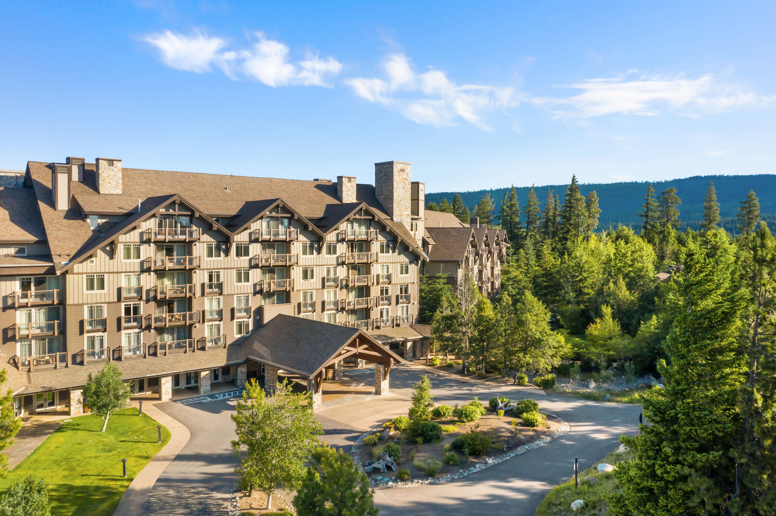 A large rustic lodge at Suncadia Resort in Washington, with peaked roofs surrounded by tall trees, set against a clear blue sky and mountains in the background. Nearby, Cle Elum restaurants provide delightful dining options for visitors to enjoy after a day of exploration.