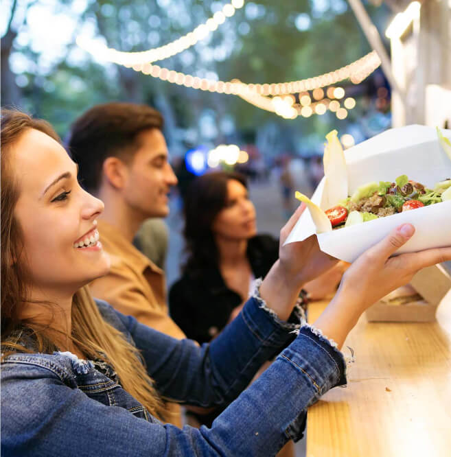 A woman smiles as she receives a food tray at an outdoor vendor stall in Suncadia, with two people standing nearby.