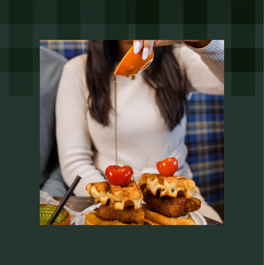 At Suncadia Resort in Washington, a person delicately pours syrup over a plate of chicken and waffles crowned with cherry tomatoes, capturing the perfect blend of savory and sweet.