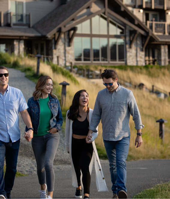 Four people walk together outdoors, smiling, in front of a large building with wooden elements at Suncadia Resort.