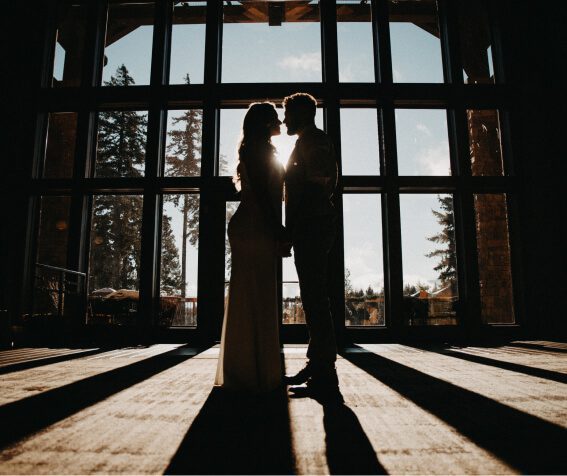 Silhouetted couple stands facing each other in front of large windows, with sunlight casting long shadows on the floor, evoking the serene beauty found in Suncadia real estate properties.