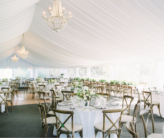 Elegant wedding reception setup under a white tent with round tables, wooden chairs, floral centerpieces, and chandeliers. The stunning backdrop of Suncadia adds a touch of natural beauty to the celebration.