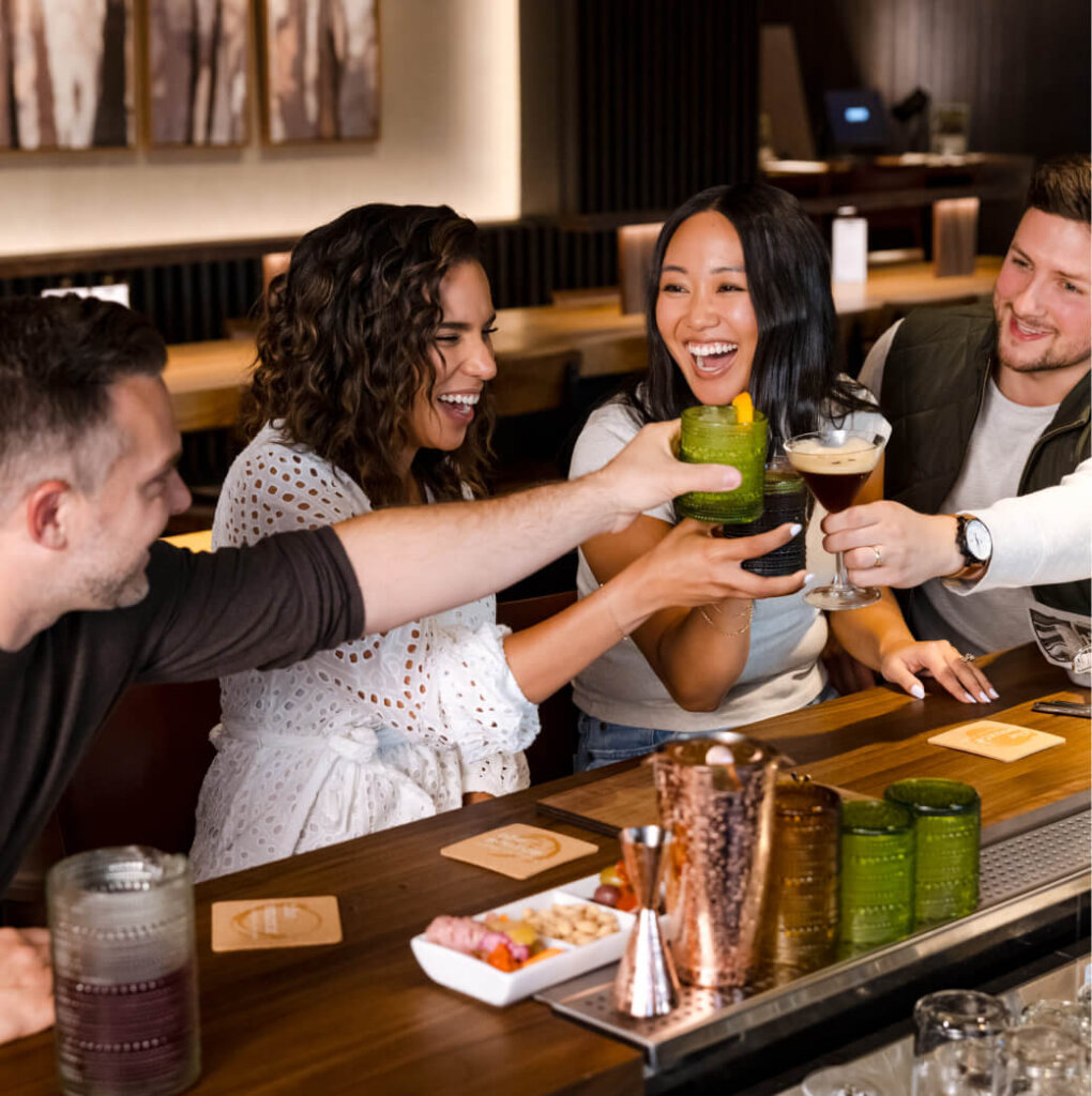 Four people clink glasses and smile while seated at a bar, enjoying the vibrant atmosphere of Suncadia Resort.