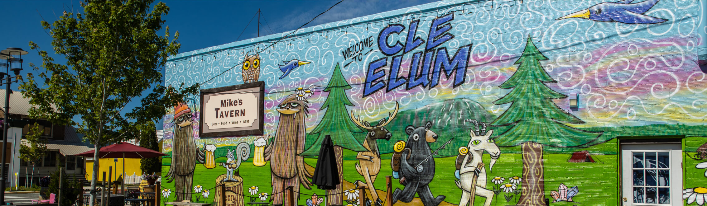 A colorful mural adorns a building with forest animals and the words "CLE ELUM," near a sign for Mike's Tavern. Just a short drive from Suncadia Resort Washington and its charming homes, it's an artistic nod to the area's vibrant community spirit.