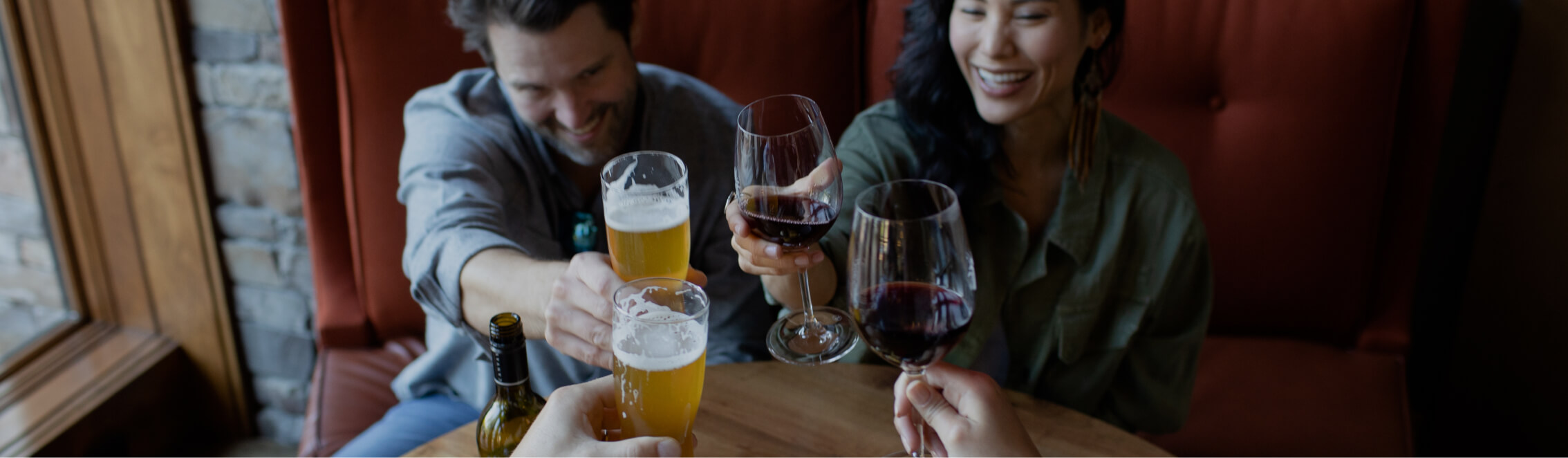 In a cozy setting at a round wooden table, three people clink glasses of wine and beer, enjoying the warm ambiance that Cle Elum restaurants are known for.