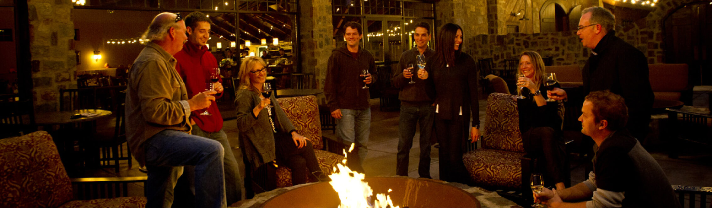 At Suncadia Resort, a group of people gather around a fire pit, holding wine glasses in the warmly lit ambiance of this inviting indoor setting.