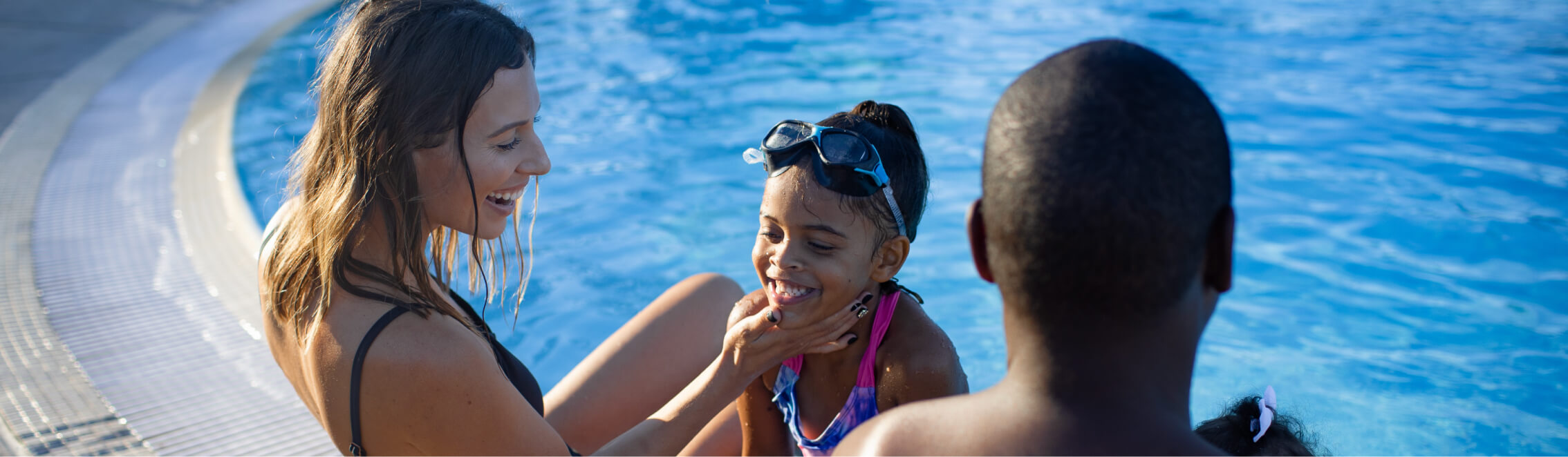 A woman and two children enjoy sitting at the edge of a swimming pool at Suncadia Resort Washington, with one child wearing goggles.