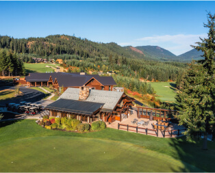 Aerial view of the Suncadia Resort's rustic lodge and surrounding golf course amidst a forested landscape, with majestic mountains in the background. Nearby, Cle Elum restaurants offer delightful dining experiences for visitors exploring Suncadia homes and the natural beauty of the area.