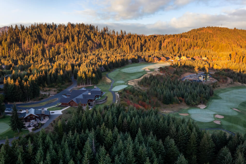 Aerial view of Suncadia Resort, Washington, showcasing a golf course nestled in dense forest beneath a partly cloudy sky. Nearby, buildings and winding roads lead to the charm of Cle Elum restaurants.