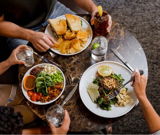 Guests at Suncadia are enjoying a delightful meal, sitting at a round table adorned with plates of salad, sandwiches accompanied by chips, and refreshing drinks.