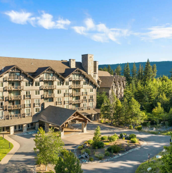 Nestled in a verdant forest under a clear blue sky, this large wooden lodge epitomizes the serene charm of Suncadia Resort. Surrounded by lush greenery, it offers an idyllic retreat within the renowned Suncadia Resort Washington.