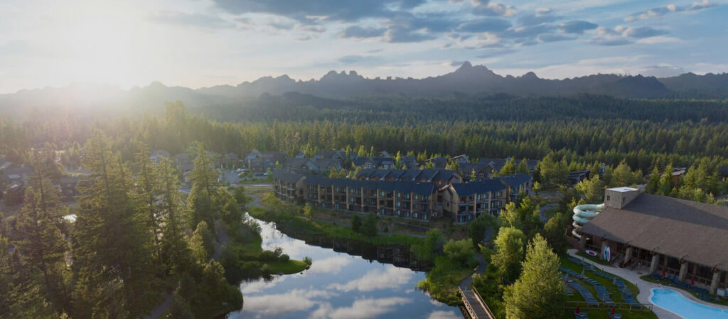 Aerial view of a resort surrounded by a forested landscape, with mountains in the background. A pond reflects the trees and Suncadia real estate, offering stunning views near Cle Elum restaurants.