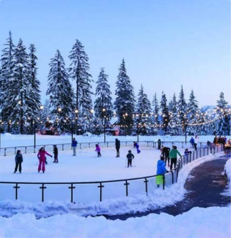 People ice skating on an outdoor rink surrounded by snow-covered trees, with string lights overhead, create a magical winter scene in Suncadia. This enchanting setting adds to the allure of discovering Suncadia real estate opportunities amidst nature's beauty.