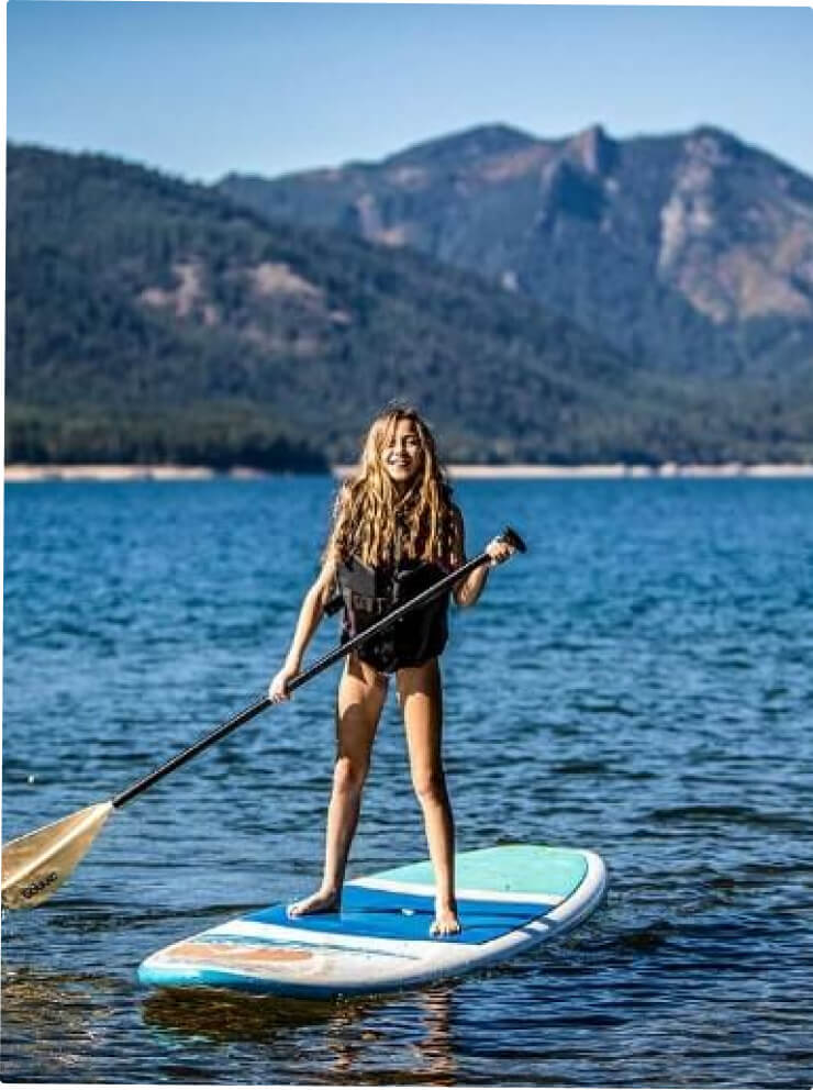 A person is paddleboarding on a blue lake with mountains in the background, not far from the welcoming charm of Cle Elum restaurants and the tranquil allure of Suncadia Resort.