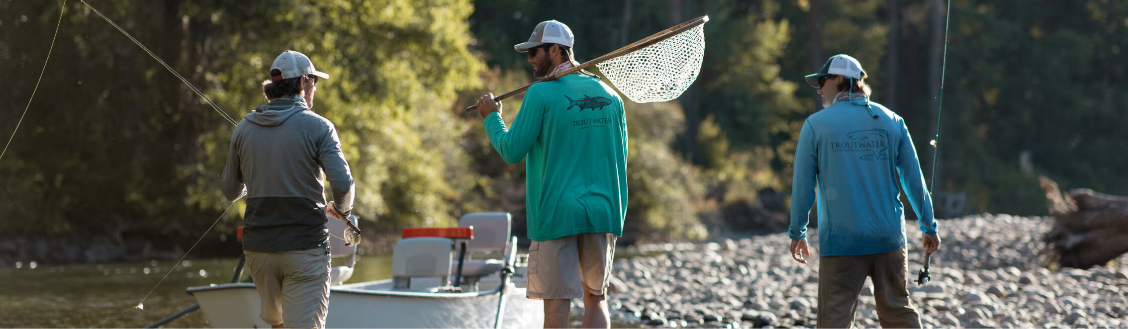 Three people wearing fishing gear stand by a river with a boat, one holding a fishing net, enjoying the serene beauty near Suncadia Resort Washington.