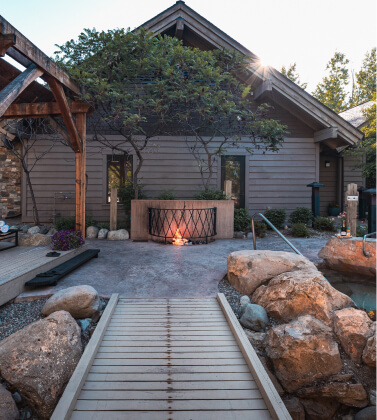 A wooden walkway leads to a building with large rocks and a fire pit in front, surrounded by trees and greenery at Suncadia Resort in Washington.