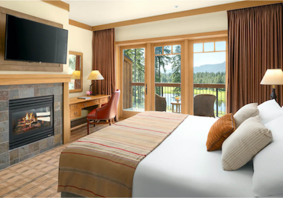 This Suncadia hotel room features a large bed, cozy fireplace, desk, and TV. Gaze out the window to see trees and distant mountains from your balcony chairs. The earth-toned decor perfectly complements the tranquil Washington setting.