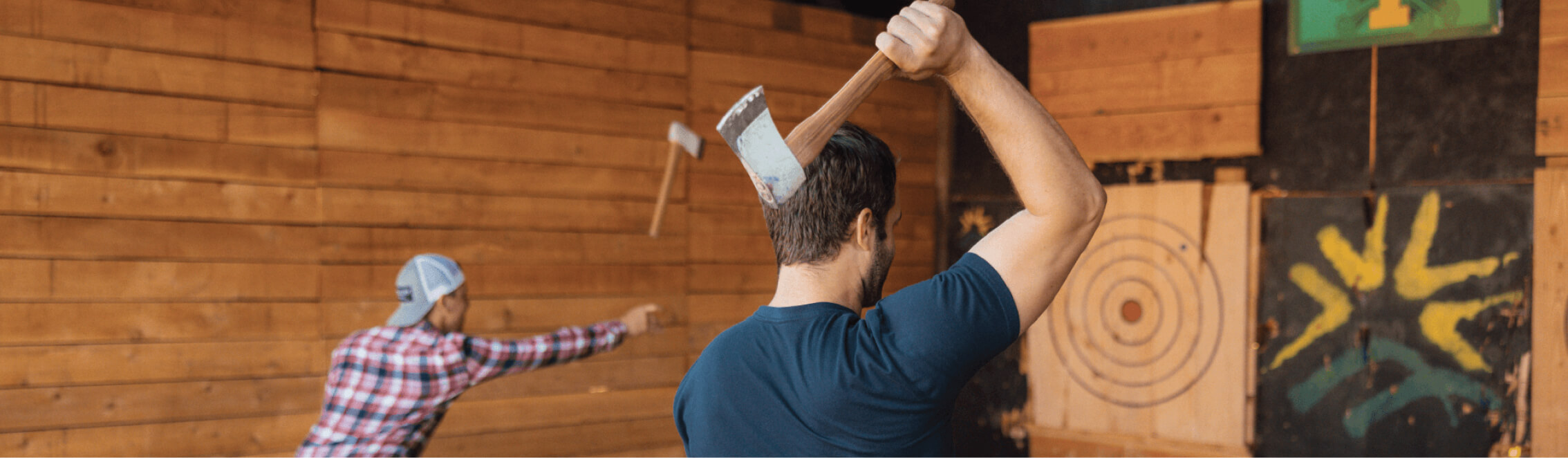 Two people throwing axes at wooden targets in an indoor range enjoy a thrilling experience at Suncadia Resort.