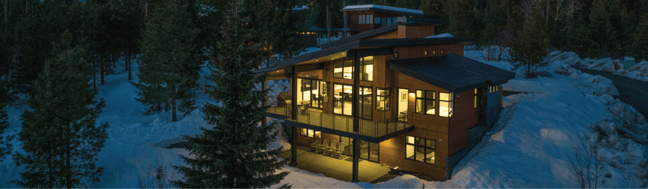 A large wooden house with illuminated windows stands surrounded by snow and trees at dusk, resembling the charming suncadia homes found near Suncadia Resort.