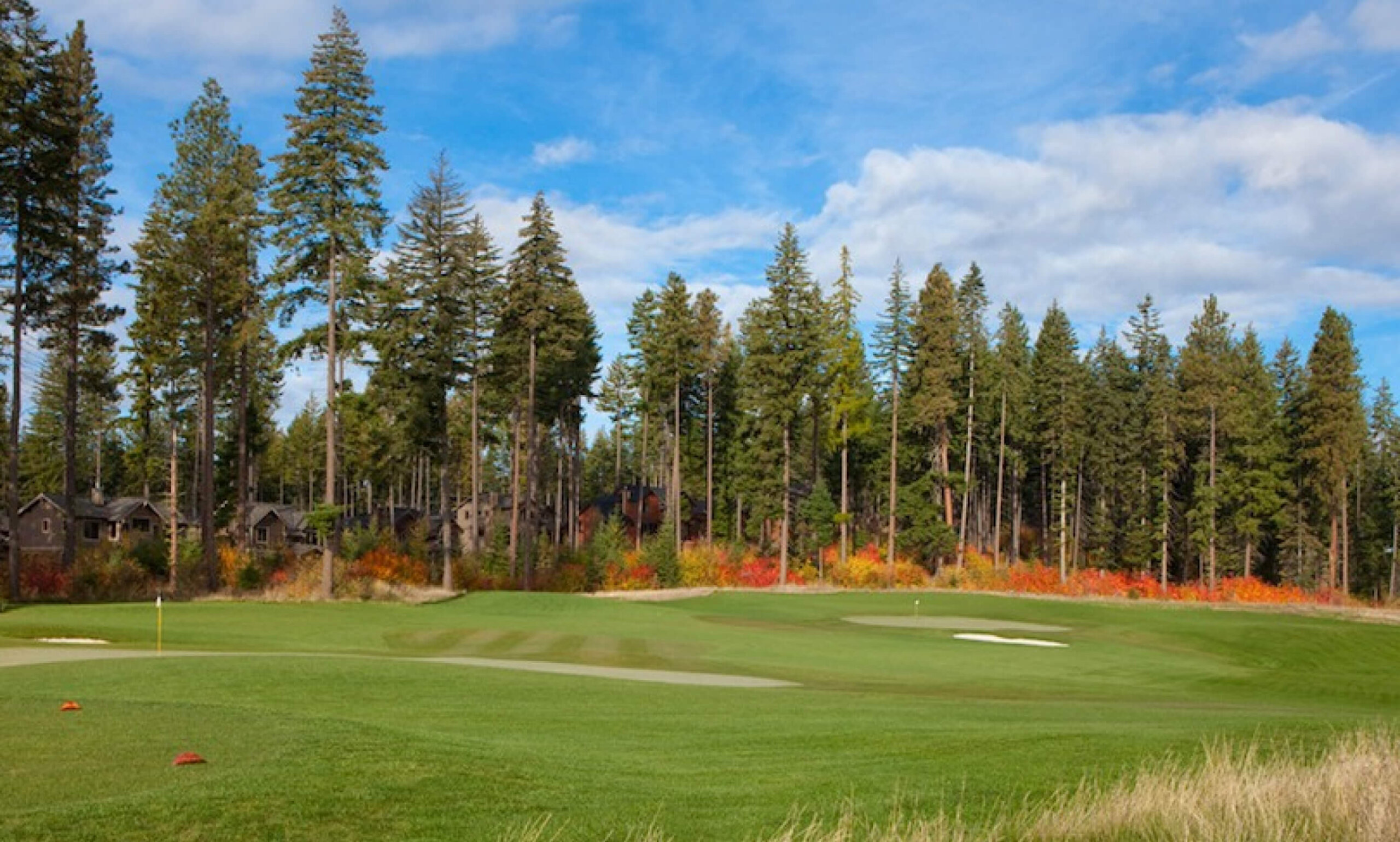 A picturesque golf course, bordered by tall trees and vibrant autumn foliage under a partly cloudy sky, embodies the charm of Suncadia Resort in Washington.