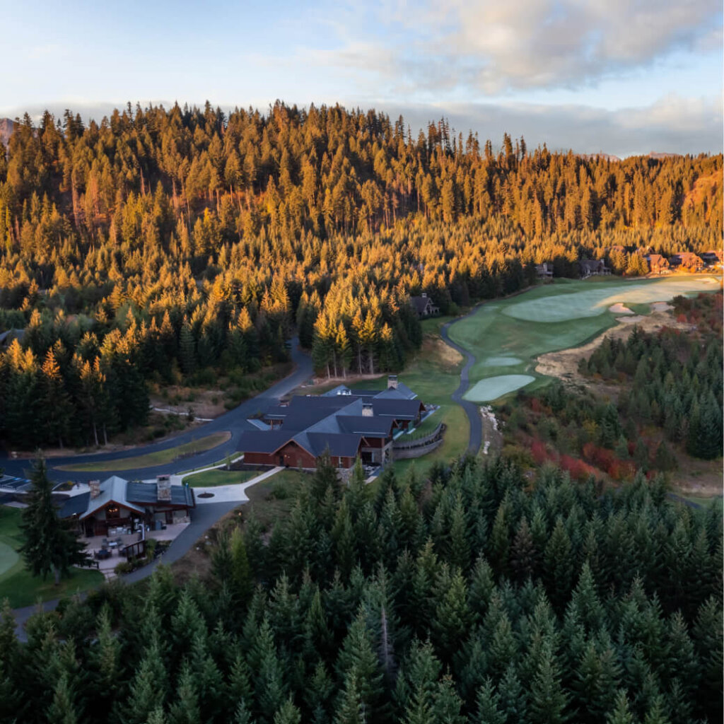 Aerial view of Suncadia Resort's clubhouse surrounded by lush forests and a golf course under a partly cloudy sky.