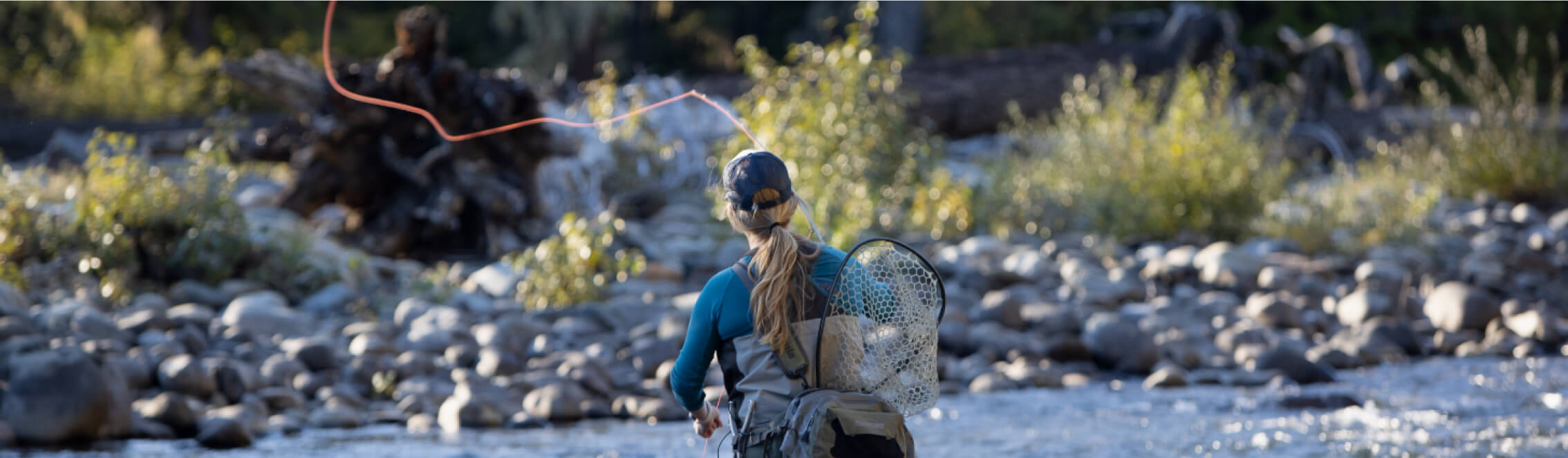 Amid the serene backdrop of a rocky river, a person gracefully fly-fishes, casting a line in perfect harmony with nature while donning a fishing vest, hat, and net. Nearby, Cle Elum restaurants await to offer delectable meals to those retreating from their outdoor adventures.