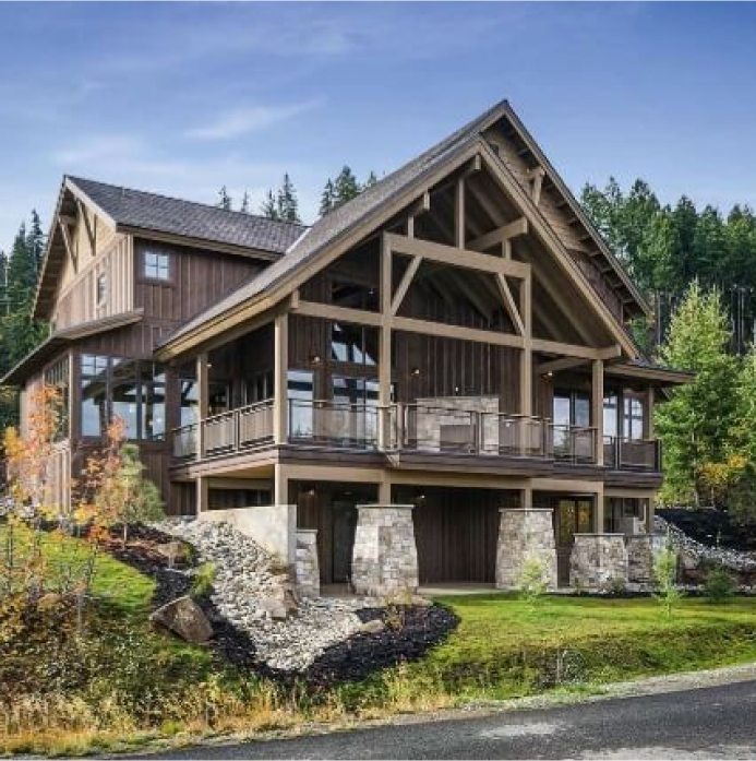 Nestled within forested hills, this large wooden house with stone accents lies under a clear blue sky, reminiscent of the picturesque retreats found near Suncadia Resort.