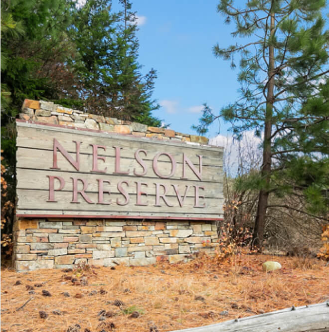 A sign reads "Nelson Preserve," surrounded by trees and lush vegetation under the clear blue skies of Suncadia Resort.