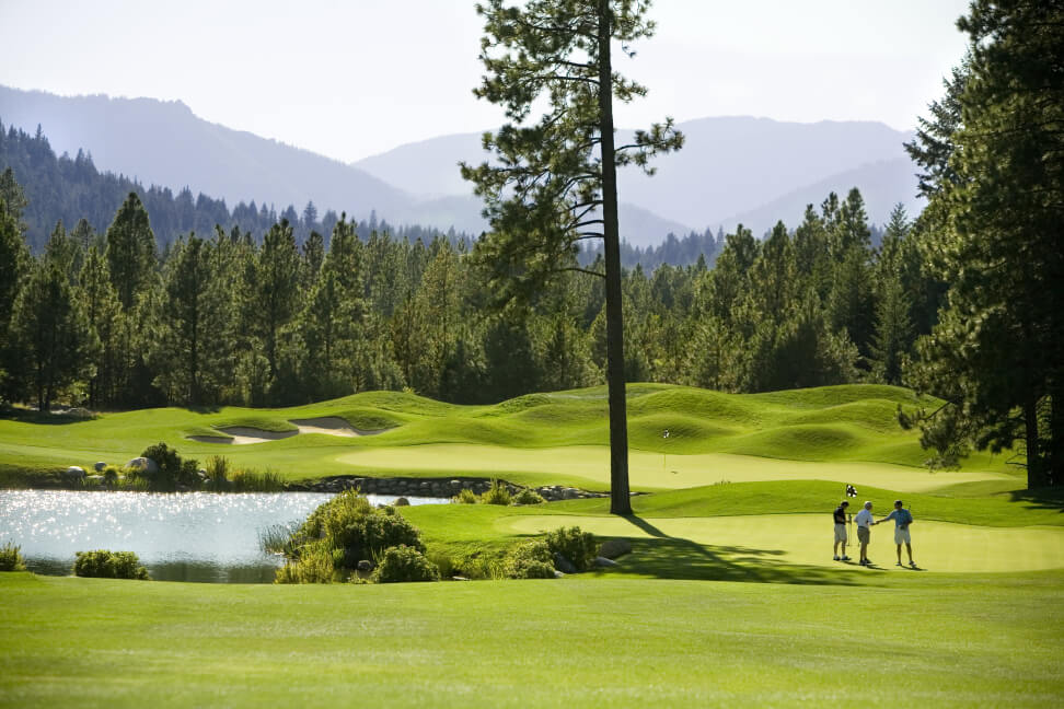 Golfers on a lush green at Suncadia, surrounded by trees and hills with a pond in the foreground under a clear sky, enjoy the serenity before indulging in fine dining at nearby Cle Elum restaurants.