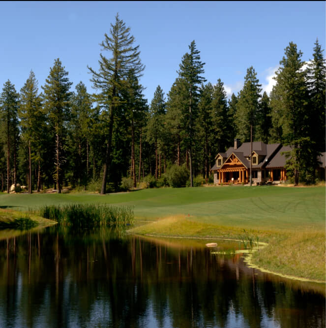 Nestled amid tall pine trees near a reflective pond, this large Suncadia home features charming wooden accents and offers a serene escape under the clear blue sky of Suncadia Resort in Washington.