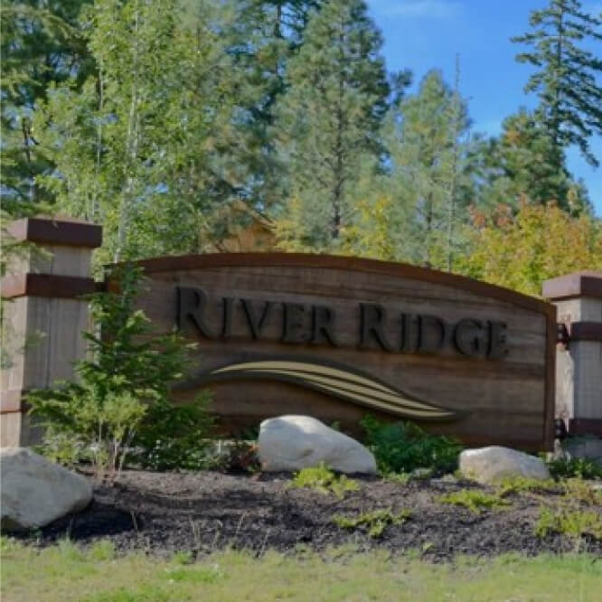 A wooden sign reads "River Ridge" amidst trees, with rocks and greenery in the foreground, echoing the serenity and charm found at Suncadia Resort.