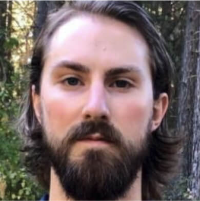 A person with a beard and long hair stands outdoors, surrounded by trees, capturing the serene essence of Suncadia Resort in Washington.