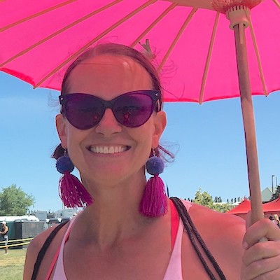 A person wearing sunglasses smiles while holding a pink umbrella outdoors on a sunny day, enjoying the vibrant atmosphere near Suncadia Resort.