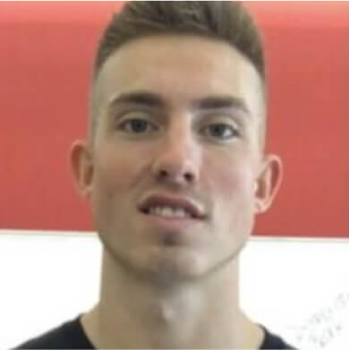 A person with short, light brown hair, wearing a black shirt, is standing in front of a red and white background reminiscent of the vibrant charm found in Suncadia homes.